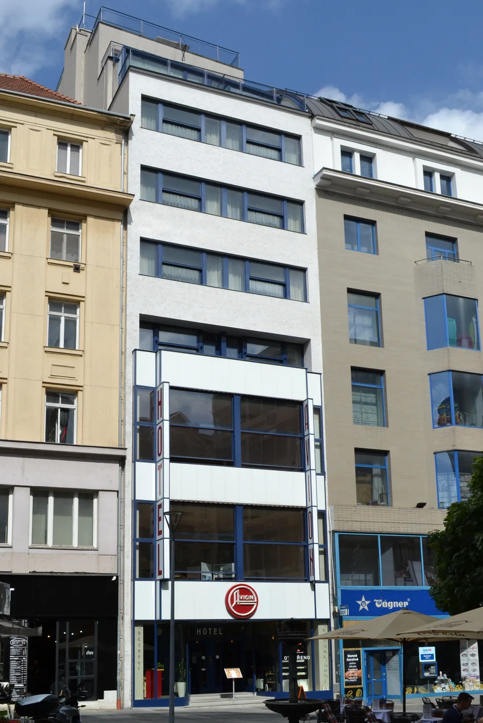 Úzká bílá fasáda hotelu Avion mezi domy v České ulici v Brně.